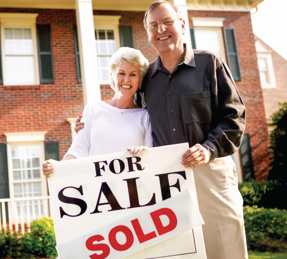 Couple holding sold sign in front of home