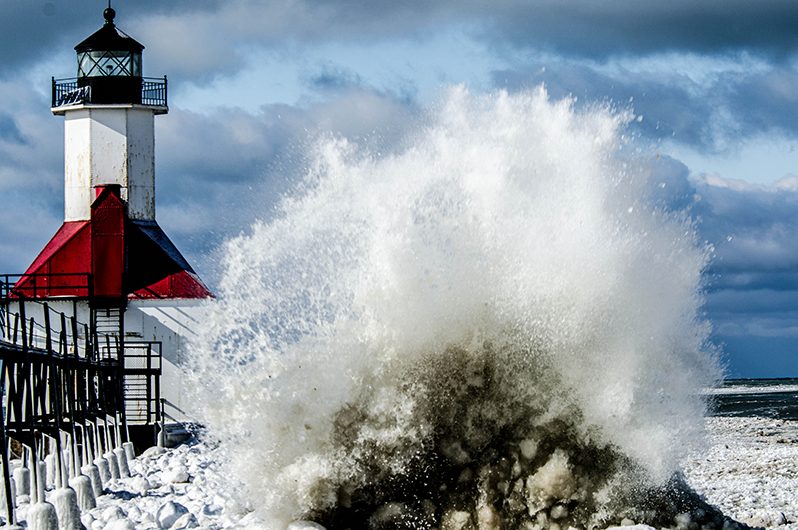 icy waves hit the beach near the light tower