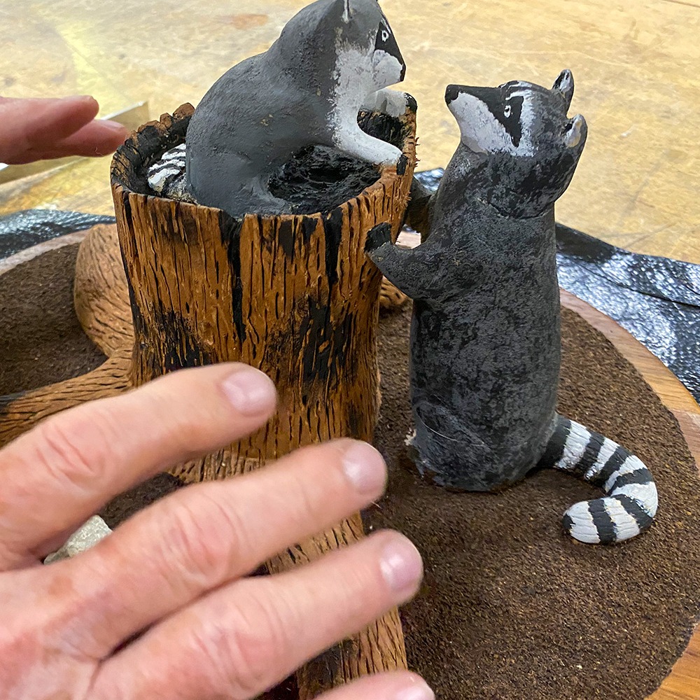 Carving of raccoons playing around a tree stump