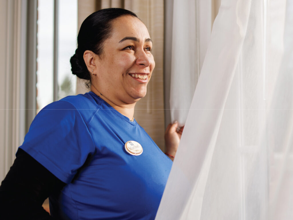 As the curtain opens and morning light pours into the well-appointed, one-bedroom Prairieview at The Garlands apartment, caregiver Maribel Lopez-Torres cheerfully belts out the classic garage rock refrain – “G  L  O  R  I  A, Gloorrr-ri-a.”