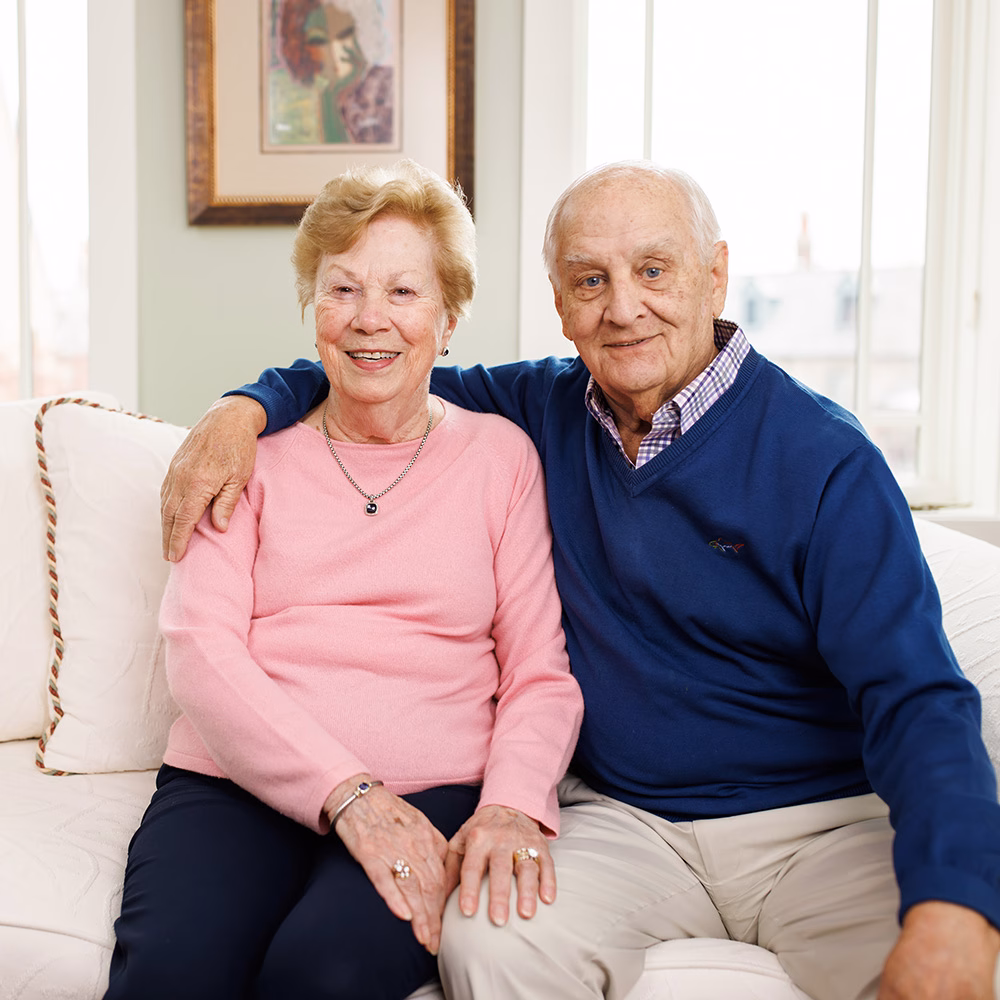 Ron and Mary Lou on their couch with his arm around her.